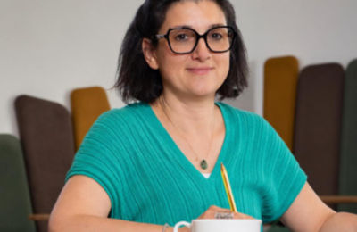 Valérie Baugé, coach professionnelle certifiée, assise à une table le stylo à la main dans une posture d'écoute active - Le rôle du coach en santé et social avec IN FINE COACHING